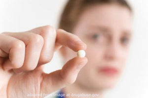 Blurred Image of Young Woman Holding Up Pill Between Her Thumb and Index Finger, adapted from image at drugabuse.gov