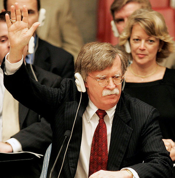 File Photo of John Bolton Raising Hand at United Nations, with United States Nameplate on Desktop in Front, adapted from image at state.gov