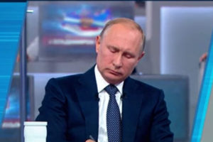 File Photo of Putin Sitting at Desk, Looking Down, Writing, During Call-In Show, adapted from screenshot of video at kremlin.ru