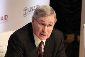 File Photo of Stephen Hadley At Table Leaning Forward, with USAID Logo Partially Obscured in Background, adapted from image at usaid.gov by Steven C. Welsh :: www.stevencwelsh.com :: www.stevencwelsh.info