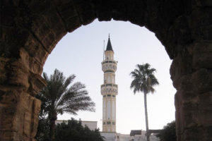 File Photo of Ancient Roman Arch in Libya Framing Minaret and Palm Trees, adapted from image at cia.gov