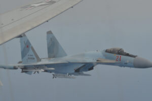 File Photo of Russian SU-35 fighter jet in flight, along with portion of wing of U.S. aircraft, adapted from image at defense.gov, with photo credit to U.S. Navy