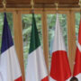 File Photo of G7 Meeting, with Persons at Round Table and Long Table, with Flags and Windows Overlooking Green Space in Background