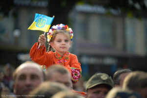 Crowd in Ukraine with Little Girl Raised Up Waving Small Ukrainian Flag, adapted from state.gov image of USAF Photo by Senior Airman Madeline Herzog