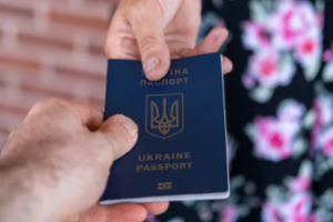 File Photo of Ukraine Passport Passed Between Hands and Lady's Dress with Brick Wall in Background, adapted from hhs.gov image